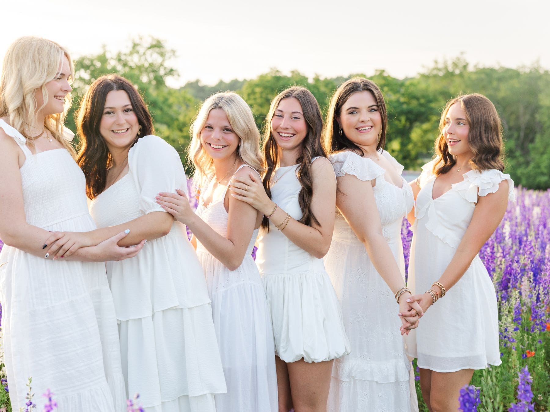 High school senior girls laughing together in a blooming larkspur field at River Bend Blooms in Kentucky.